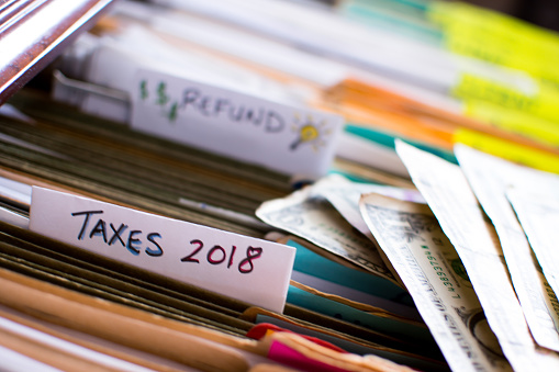 Tax refund conceptual tax season tax preparation photography with files and tax forms in filing cabinet and words refund and taxes 2018 written on file folders  with light bulb for ideas and US dollar cash in background