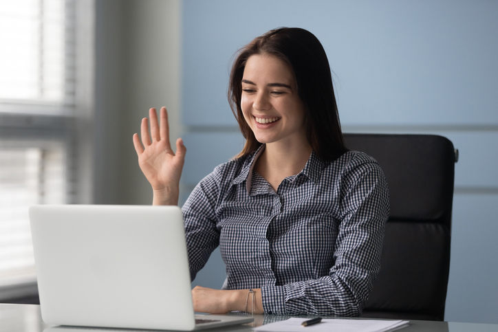 Happy young businesswoman holding video call with clients or greeting partners at workplace. Smiling millennial trainer speaker recording educational webinar lecture, waving hello to participants.